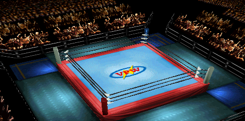 Screenshot of Kawasaki Stadium, focused
on the ring area. Fans can be seen on three of the four sides. Guardrails (using a
sparser design) separate the fans from ringside. The outside corners are deep blue
mats, while the mats around the ring are a lighter blue. The ring mat design consists
of a blue square surrounded by a red border. The same shade of red extends to the
ring skirt. In the center of the ring is a logo consisting of a blue oval, yellow
sideways lightning bolt, and red 'VPW' text (in a block serif typeface).