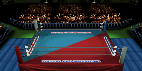 Screenshot of Nippon Budokan, focused on the
ring area. The upper middle portion contains cheering fans behind a row of guardrails.
Guardrails also appear on the left and right side, but disappear shortly due to the
perspective. A wrestling ring is the central focus, featuring a two-tone ring mat
design. The design is split on a diagonal, with the upper left portion being teal,
and the lower right portion being a dark red. 'VIRTUAL PRO-WRESTLING' text appears
on the four cardinal edges of the ring mat. The text has a white stroke, while the
fill color depends on the text location (blue fill for the red mat portion, red fill
for the cyan mat portion). Outside of the ring, blue padded mats appear to the left
and right. The outside corners are green and lack mats.